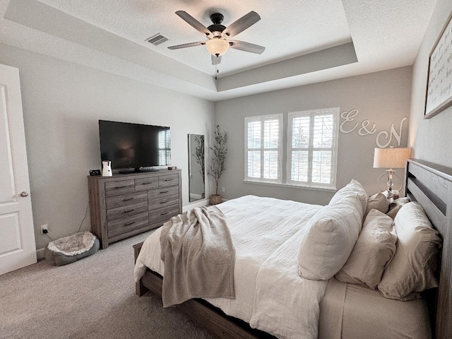 bedroom with ceiling fan, a tray ceiling, carpet floors, and a textured ceiling