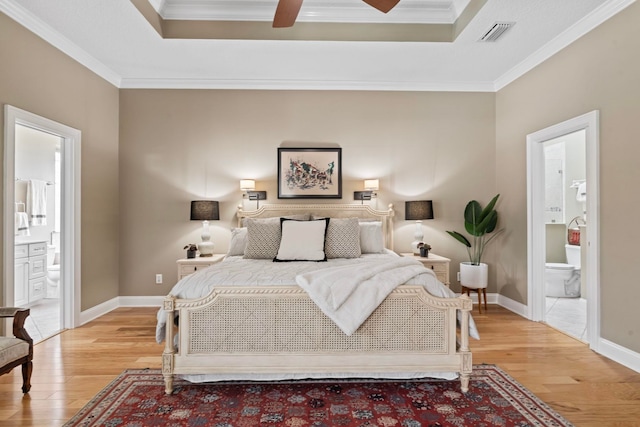 bedroom with light hardwood / wood-style flooring, crown molding, ensuite bath, and a raised ceiling