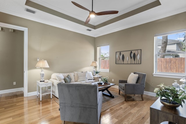 living room featuring ceiling fan, ornamental molding, a tray ceiling, and light hardwood / wood-style floors