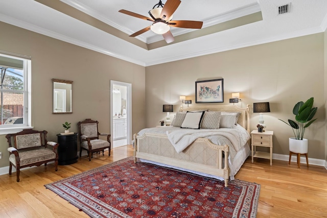 bedroom featuring wood-type flooring, ornamental molding, connected bathroom, and a tray ceiling