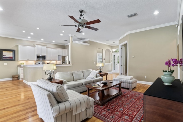 living room featuring ornamental molding, ceiling fan, a textured ceiling, and light hardwood / wood-style floors