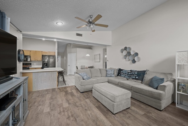 living room with a textured ceiling, ceiling fan, light hardwood / wood-style flooring, and vaulted ceiling