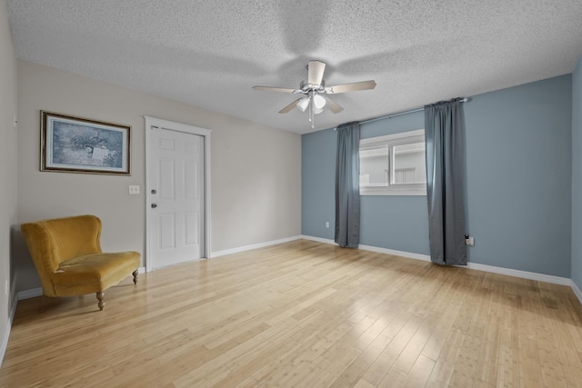 empty room with ceiling fan, light wood-type flooring, and a textured ceiling