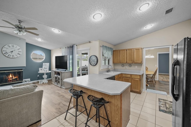 kitchen with kitchen peninsula, light wood-type flooring, black fridge, a textured ceiling, and vaulted ceiling