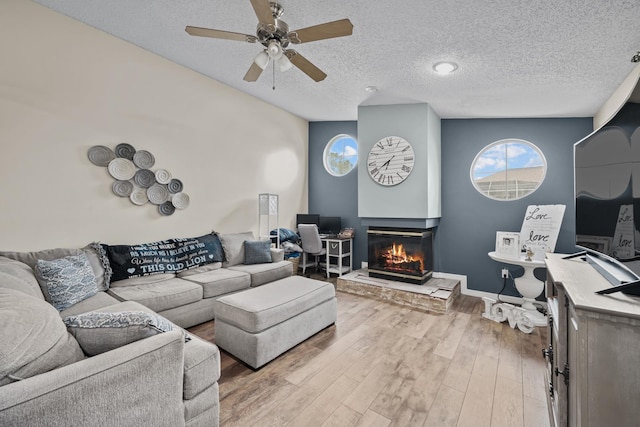 living room featuring ceiling fan, a multi sided fireplace, hardwood / wood-style floors, vaulted ceiling, and a textured ceiling