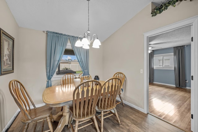 dining space with hardwood / wood-style floors, ceiling fan with notable chandelier, lofted ceiling, and a textured ceiling