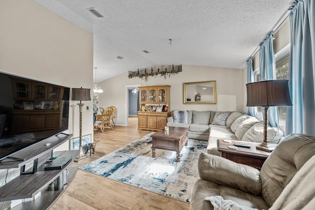 living room with a textured ceiling, light hardwood / wood-style flooring, a chandelier, and vaulted ceiling