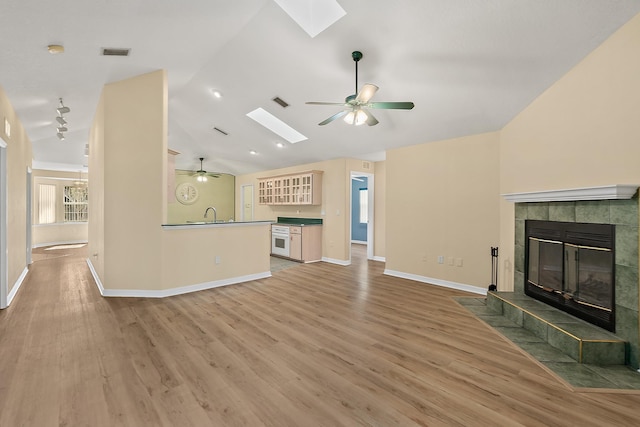 76 Kakakee Trl, Palm Coast, FL 32164 - unfurnished living room featuring a skylight, a ceiling fan, lofted ceiling, a tiled fireplace, and light wood-type flooring