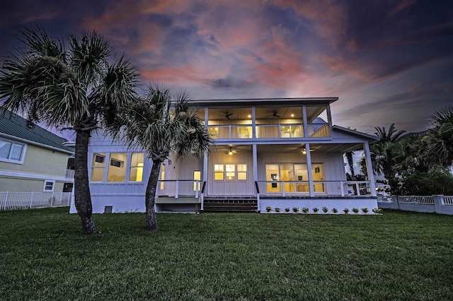 back house at dusk featuring a lawn, ceiling fan, a balcony, and a porch