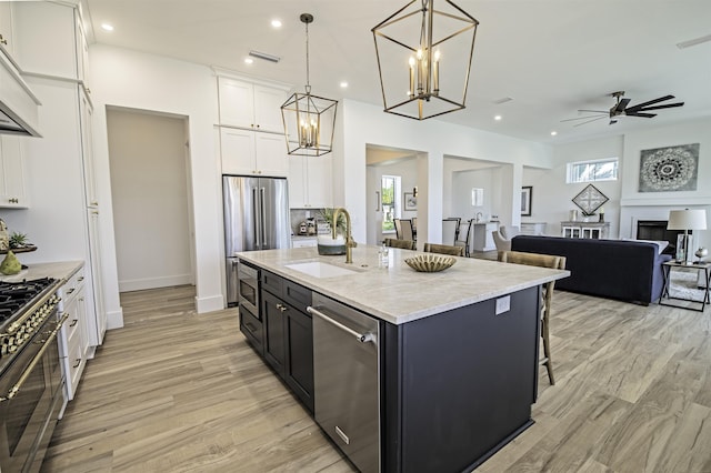 kitchen with appliances with stainless steel finishes, a kitchen island with sink, sink, decorative light fixtures, and white cabinetry