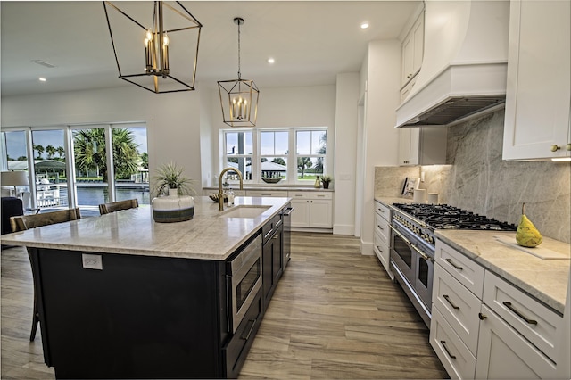 kitchen with white cabinets, appliances with stainless steel finishes, a kitchen island with sink, and custom exhaust hood