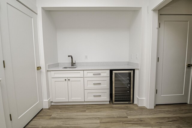 bar with white cabinetry, sink, beverage cooler, and light hardwood / wood-style floors