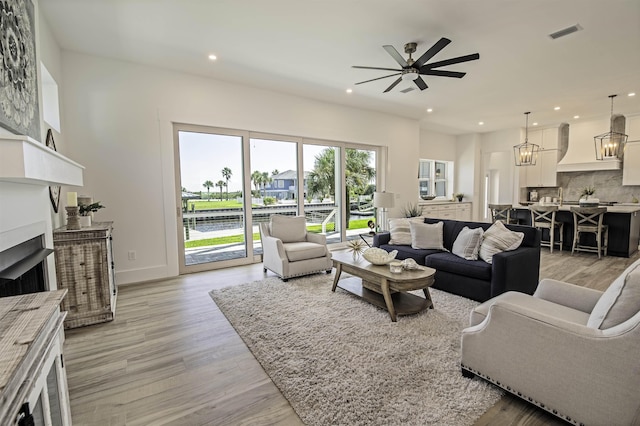 living room featuring ceiling fan with notable chandelier and light wood-type flooring