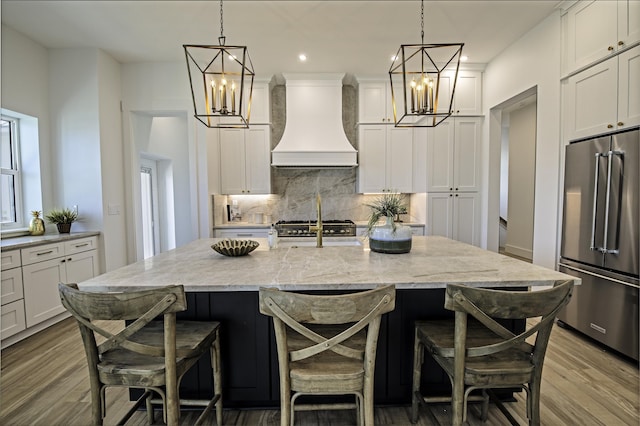 kitchen with a kitchen breakfast bar, decorative light fixtures, a kitchen island with sink, custom range hood, and appliances with stainless steel finishes