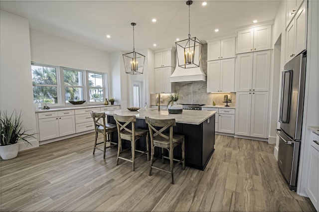 kitchen featuring a center island with sink, white cabinets, custom range hood, and appliances with stainless steel finishes