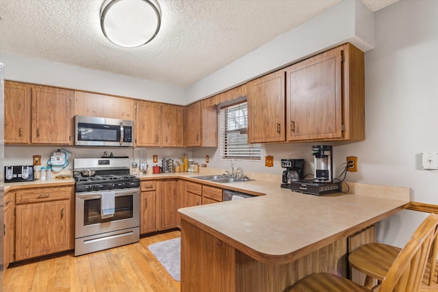 kitchen with sink, stainless steel appliances, light hardwood / wood-style floors, a kitchen bar, and kitchen peninsula