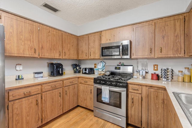 kitchen with stainless steel appliances, sink, a textured ceiling, and light hardwood / wood-style flooring