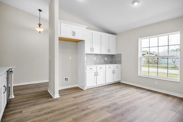 kitchen with tasteful backsplash, light hardwood / wood-style floors, white cabinets, decorative light fixtures, and vaulted ceiling