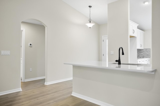 kitchen with sink, white cabinetry, tasteful backsplash, decorative light fixtures, and light wood-type flooring