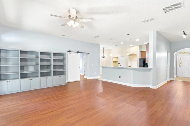 unfurnished living room featuring a textured ceiling, light hardwood / wood-style flooring, a barn door, and ceiling fan