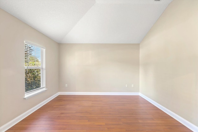 unfurnished room featuring wood-type flooring, a textured ceiling, and vaulted ceiling