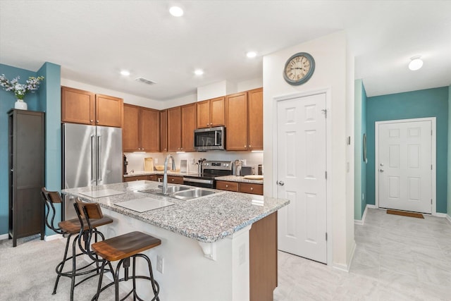 kitchen featuring sink, a kitchen breakfast bar, an island with sink, stainless steel appliances, and light stone countertops