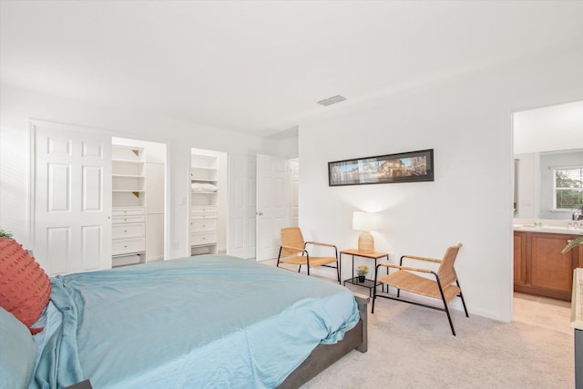 bedroom featuring light carpet, ensuite bath, a walk in closet, and a closet