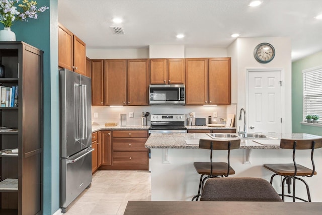 kitchen featuring appliances with stainless steel finishes, sink, a kitchen breakfast bar, a kitchen island with sink, and light stone counters