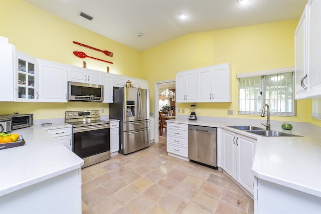 kitchen featuring appliances with stainless steel finishes, lofted ceiling, white cabinetry, sink, and a notable chandelier