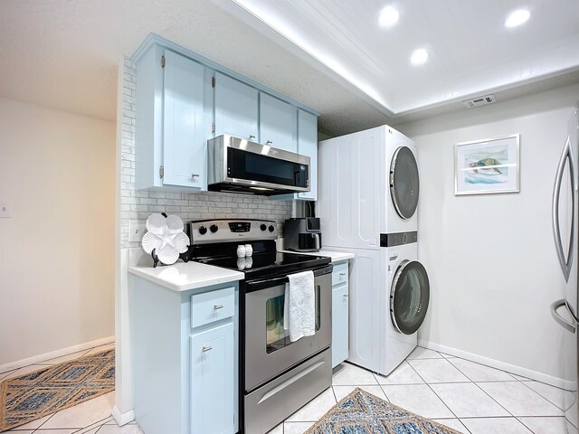 kitchen with light tile patterned flooring, backsplash, stacked washer / dryer, white cabinets, and appliances with stainless steel finishes