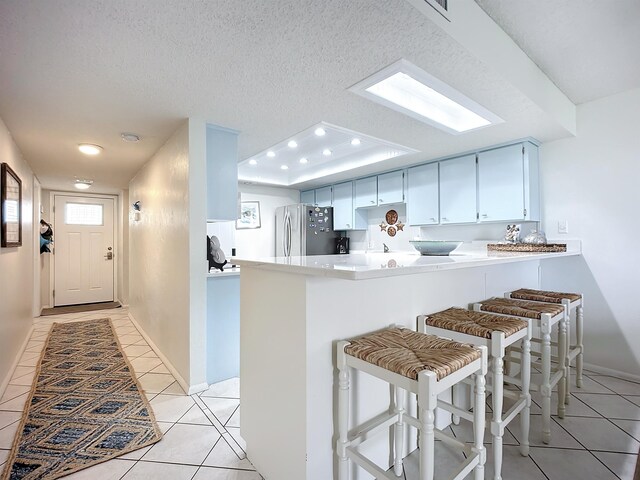 kitchen with a kitchen breakfast bar, light tile patterned floors, a textured ceiling, kitchen peninsula, and stainless steel refrigerator