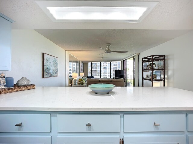 kitchen featuring a skylight, light stone countertops, ceiling fan, and a textured ceiling