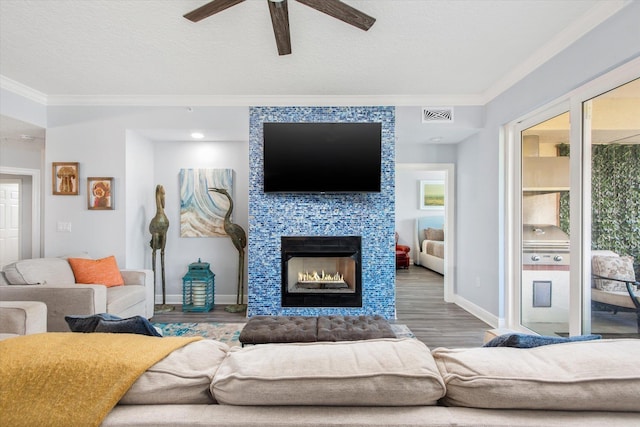 living area with visible vents, a tiled fireplace, wood finished floors, a textured ceiling, and crown molding