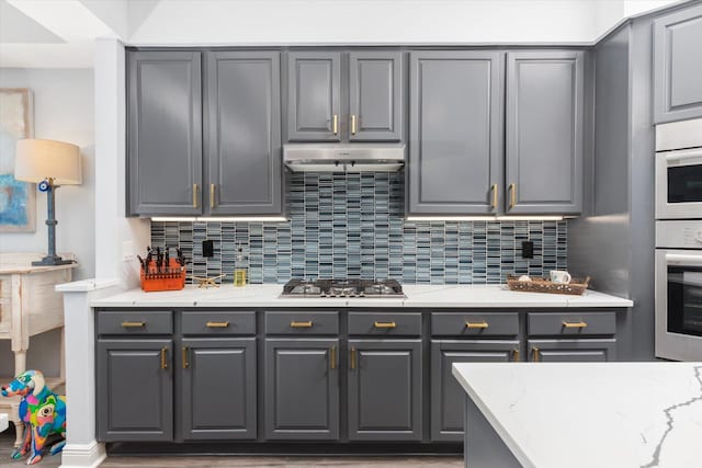 kitchen featuring stainless steel gas cooktop, tasteful backsplash, gray cabinetry, and under cabinet range hood