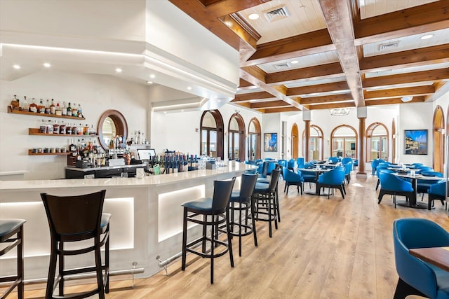 bar with beam ceiling, a dry bar, visible vents, light wood-style flooring, and coffered ceiling