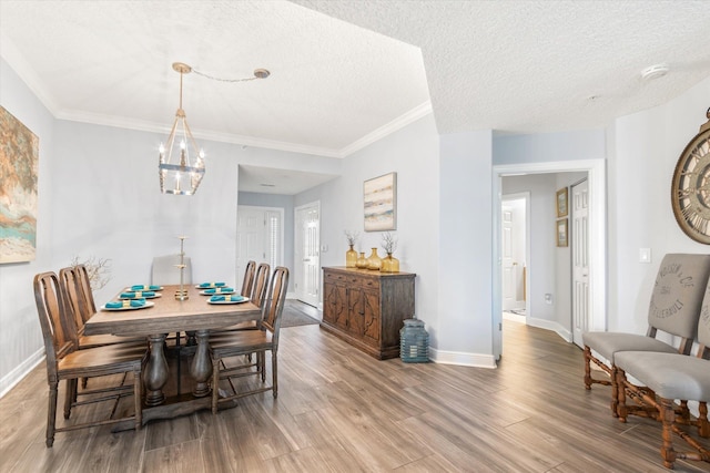 dining area with a notable chandelier, ornamental molding, a textured ceiling, wood finished floors, and baseboards