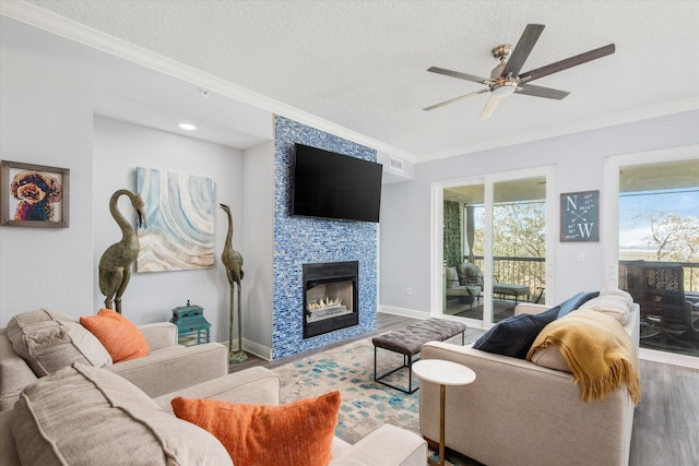 living room featuring baseboards, a tiled fireplace, ornamental molding, wood finished floors, and a textured ceiling