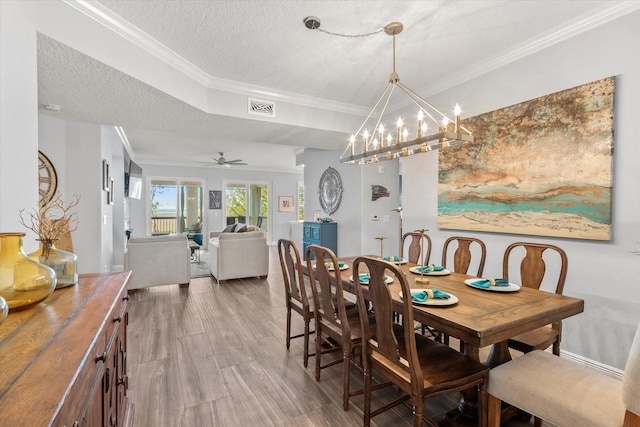 dining space featuring visible vents, ornamental molding, wood finished floors, a textured ceiling, and ceiling fan with notable chandelier