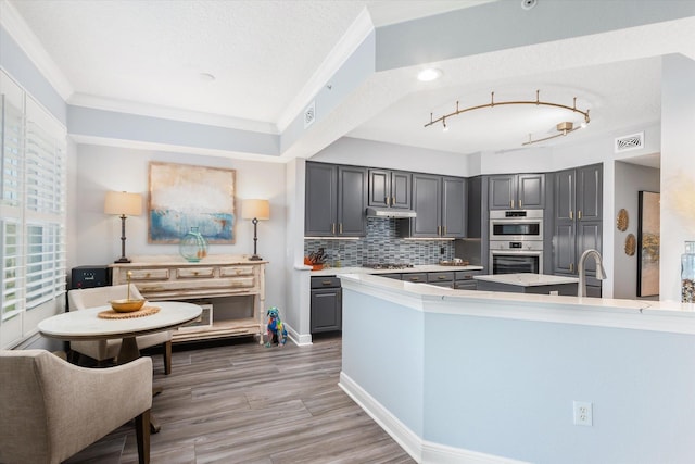 kitchen featuring tasteful backsplash, visible vents, gray cabinetry, a sink, and under cabinet range hood