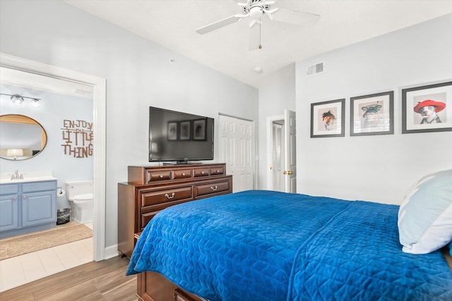 bedroom featuring a sink, wood finished floors, visible vents, a ceiling fan, and ensuite bath