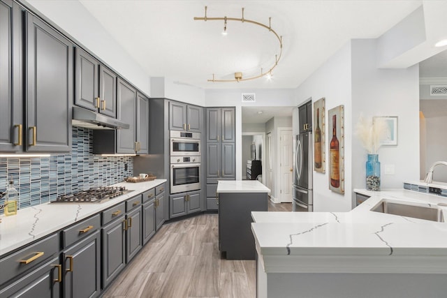 kitchen with tasteful backsplash, appliances with stainless steel finishes, gray cabinetry, under cabinet range hood, and a sink