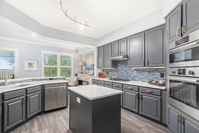 kitchen with appliances with stainless steel finishes, a sink, gray cabinets, under cabinet range hood, and backsplash