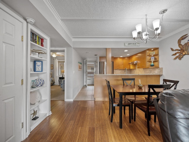 dining space with a textured ceiling, light hardwood / wood-style floors, an inviting chandelier, and ornamental molding