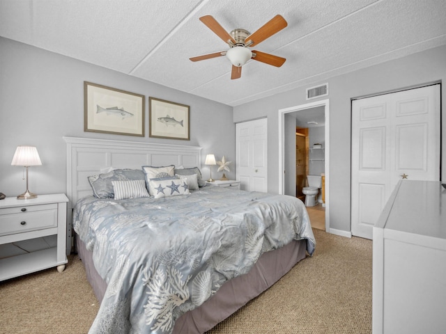 bedroom with a textured ceiling, light colored carpet, ensuite bath, and ceiling fan