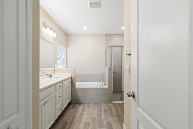 full bathroom featuring double vanity, visible vents, a garden tub, wood finish floors, and a shower stall