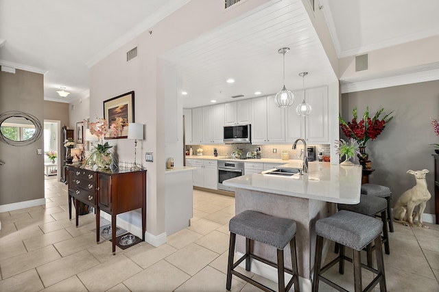 kitchen with white cabinetry, sink, hanging light fixtures, appliances with stainless steel finishes, and ornamental molding