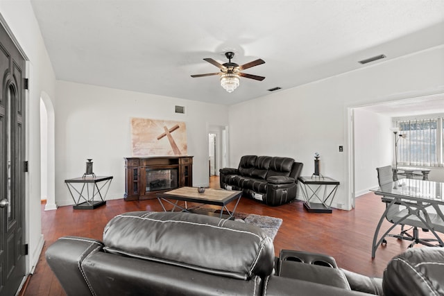 living area featuring arched walkways, dark wood-type flooring, a glass covered fireplace, and visible vents