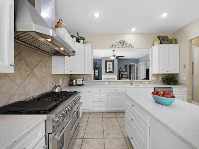 304 1st St, Saint Augustine, FL 32084 - kitchen with wall chimney range hood, stainless steel appliances, decorative backsplash, white cabinets, and a ceiling fan