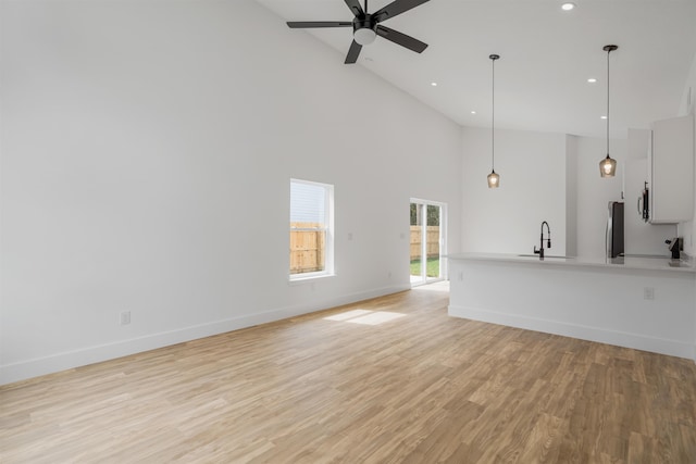 unfurnished living room featuring ceiling fan, light hardwood / wood-style floors, sink, and high vaulted ceiling