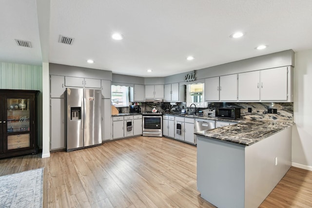 kitchen featuring tasteful backsplash, kitchen peninsula, dark stone counters, light hardwood / wood-style floors, and appliances with stainless steel finishes